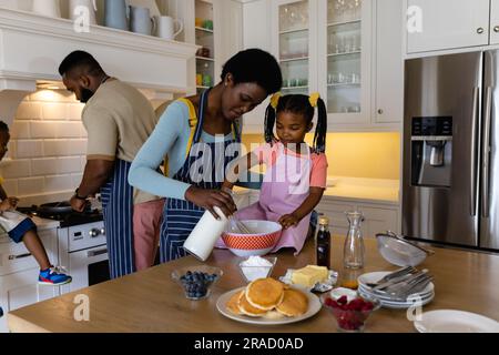 Mère et fille afro-américaines mélangeant la pâte dans un bol tandis que père et fils font des crêpes Banque D'Images