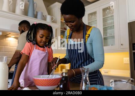 Mère et fille afro-américaines mélangeant la pâte dans un bol sur la table dans la cuisine Banque D'Images
