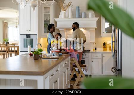 Frères et sœurs afro-américains mélangeant la pâte dans un bol sur un îlot de cuisine avec des parents en arrière-plan à la maison Banque D'Images