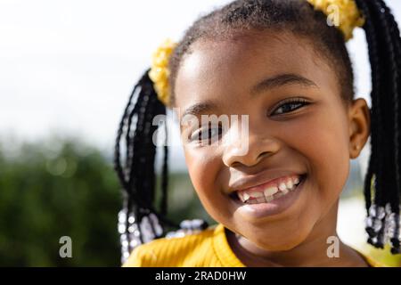 Gros plan portrait de mignonne fille afro-américaine souriant à la caméra contre ciel clair dans la cour Banque D'Images