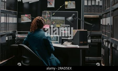 Une femme chargée de la loi prend des notes sur les dossiers, tente de résoudre le crime et de trouver un suspect. Détective professionnel regardant des photos de preuves et des déclarations de témoins, expertise judiciaire. Banque D'Images