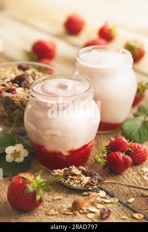 Délicieux yaourt aux fraises en pots et granola entouré de baies fraîches sur la table rustique en bois. Concept de petit déjeuner sain avec fraise A. Banque D'Images