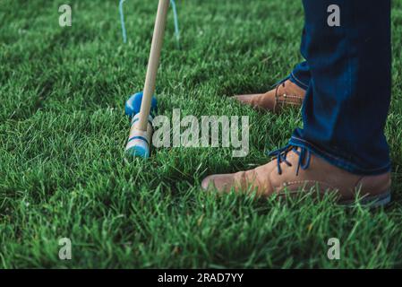 Gros plan des pieds se tenant à côté du maillet de croquet et de la balle dans l'herbe. Banque D'Images