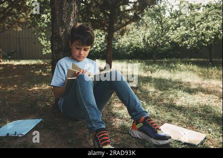 Adorable adolescent, écolier lisant un livre assis sous un arbre dans le parc. École. Éducation. Adolescence d'enfance Banque D'Images