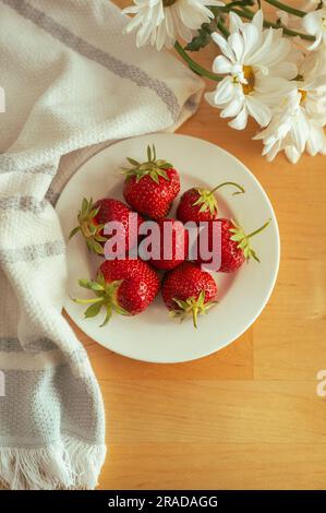 des fraises biologiques fraîchement cueillies sur l'assiette, accompagnées de fleurs blanches et d'une serviette Banque D'Images