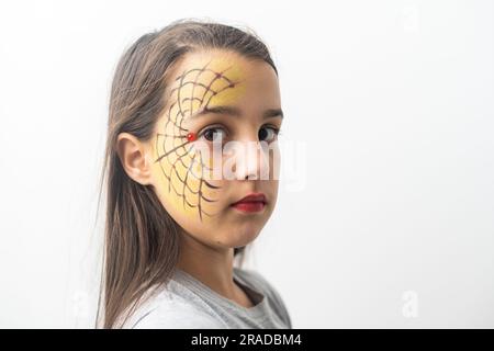 Belle fille adolescente aux yeux bruns, cheveux longs, sourire et regarder vers le bas dans un chapeau vert avec araignées noires et toile pour la fête de costume, avec maquillage d'eau Banque D'Images