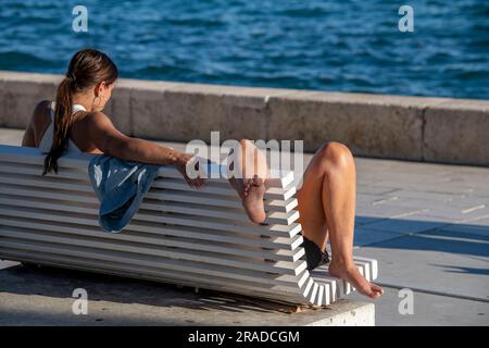 jeune femme assise sur un banc se détendant dans le chaud soleil d'été, paire de jambes sortant du bout d'un banc, endormie au soleil Banque D'Images