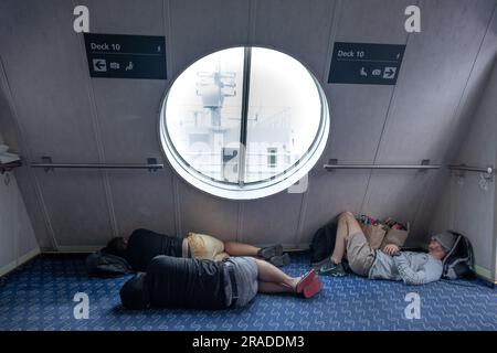 Les voyageurs dormant sur le sol dans un couloir sur une traversée en ferry de Wellington à Picton bondée de l'île du Nord à l'île du Sud, en Nouvelle-Zélande Banque D'Images