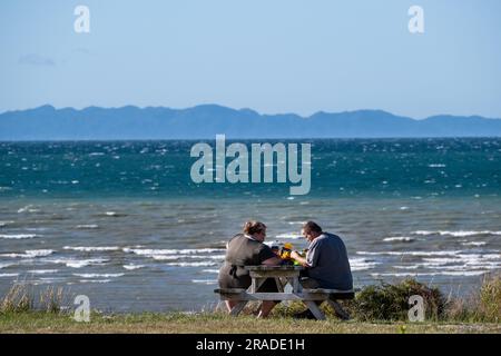 Un couple obèse partage un pique-nique sur la plage dans la région côtière de Takaka sur Golden Bay près du parc national Abel Tasman sur l'île du Sud, en Nouvelle-Zélande. Banque D'Images