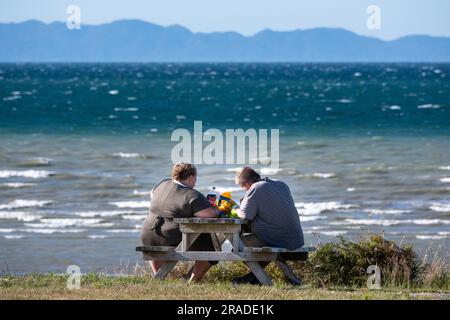 Un couple obèse partage un pique-nique sur la plage dans la région côtière de Takaka sur Golden Bay près du parc national Abel Tasman sur l'île du Sud, en Nouvelle-Zélande. Banque D'Images