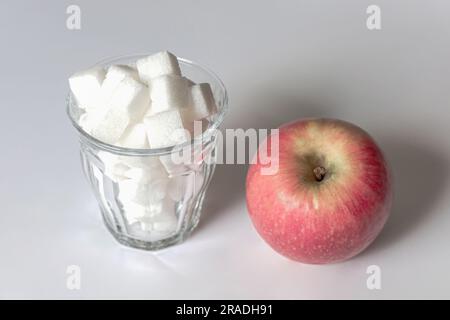 Plein verre de sucre et pomme rouge. Concept de choix entre aliments sains et malsains. Banque D'Images