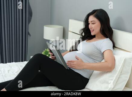 femme enceinte utilisant un comprimé numérique sur un lit Banque D'Images