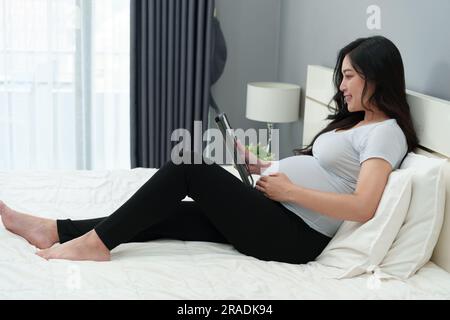 femme enceinte utilisant un comprimé numérique sur un lit Banque D'Images