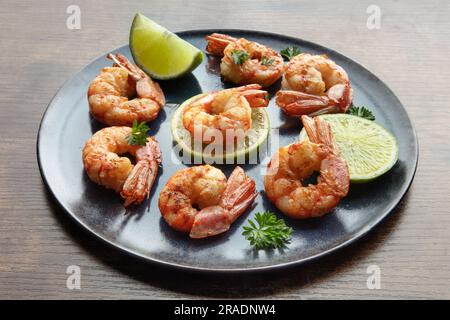 Crevettes avec des limes et du persil. Crevettes grillées sur une table rustique. Hors-d'œuvre de fruits de mer épicés Banque D'Images