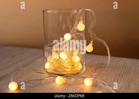 Guirlande de boules de lumières jaunes dans un pot en verre sur fond de table en bois clair. Guirlande lumineuse de Noël jaune or avec ampoules LED. La guirlande du nouvel an. FR Banque D'Images