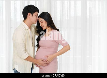 mari embrassant le front de sa femme enceinte près de la fenêtre. couple amour concept Banque D'Images