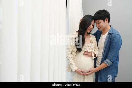 le couple marié attend bébé. l'homme embrasse sa femme enceinte près de la fenêtre Banque D'Images