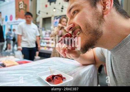 Le touriste mange du tako tamago, poulpe avec un œuf dans la tête, à Osaka, Japon. Banque D'Images