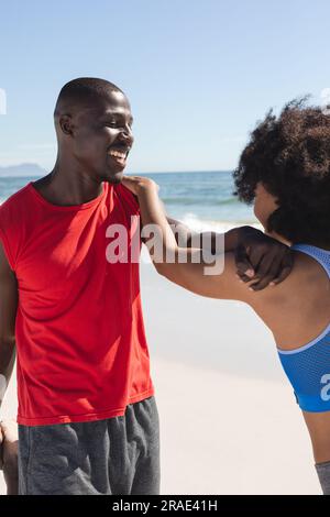Heureux, en forme couple afro-américain s'exerçant, s'étirant et souriant sur la plage ensoleillée Banque D'Images