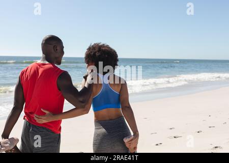 Heureux, en forme couple afro-américain s'exerçant, s'étirant et embrassant sur la plage ensoleillée, espace de copie Banque D'Images