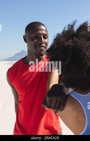Heureux, en forme couple afro-américain s'exerçant, s'étirant et souriant sur la plage ensoleillée Banque D'Images