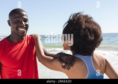 Heureux, en forme couple afro-américain s'exerçant, s'étirant et souriant sur la plage ensoleillée Banque D'Images