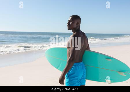 FIT homme afro-américain tenant la planche de surf sur la plage ensoleillée, regardant loin Banque D'Images