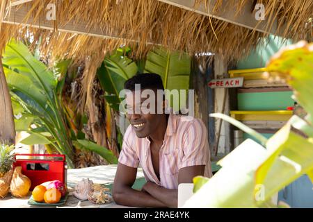 Portrait de l'homme afro-américain heureux appuyé sur le comptoir de la cabane de plage de location de surf Banque D'Images