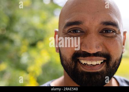 Demi-portrait d'homme biracial chauve souriant avec barbe devant la cime des arbres, espace de copie Banque D'Images