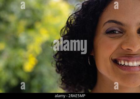 Demi-portrait de femme biracial souriante avec les cheveux noirs bouclés devant la cime des arbres, espace de copie Banque D'Images