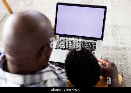 Grand-père et petit-fils afro-américains assis sur le canapé, en utilisant un ordinateur portable avec espace de copie sur l'écran Banque D'Images