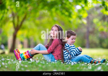 Joyeux enfants garçon et fille en bottes de caoutchouc de pluie jouant à l'extérieur dans le parc vert avec champ fleuri de fleurs de Marguerite Banque D'Images