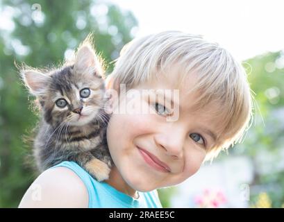 visage d'un garçon heureux de 6-7 ans sur l'épaule d'un petit chaton bien-aimé à rayures. journée du chat. Bonne enfance avec un animal de compagnie moelleux. Position douce Banque D'Images