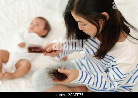 mère stressée ayant un problème de perte de cheveux post-partum avec son bébé à la maison Banque D'Images