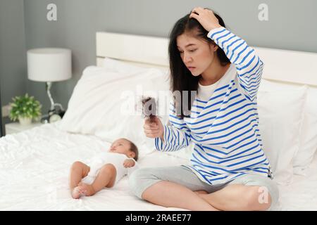 mère stressée ayant un problème de perte de cheveux post-partum avec son bébé à la maison Banque D'Images