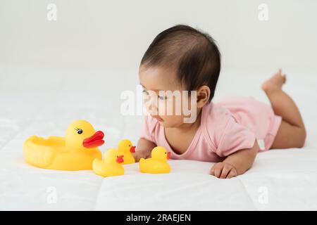 bébé jouant avec un jouet de canard en caoutchouc jaune sur un lit Banque D'Images