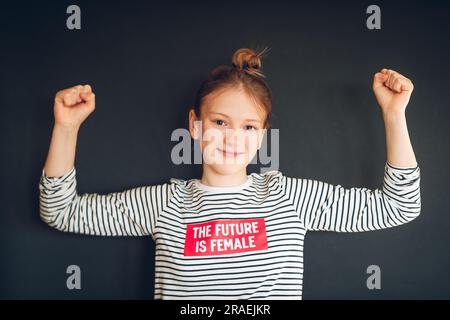 Photo de studio de jeune fille forte de la préadolescence fléchissant les muscles des bras, portant un t-shirt avec le slogan « future is female » Banque D'Images