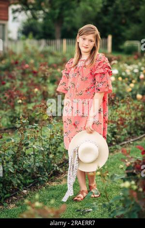 Portrait d'été de la jolie petite fille portant une robe à rayures rouges, posant dans un jardin de roses Banque D'Images