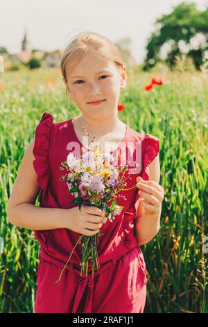 Portrait extérieur d'adorable petite fille avec bouquet de fleurs sauvages Banque D'Images