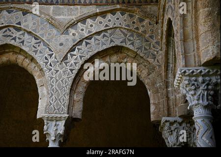 Arches et colonnes de style normand arabesques avec chapiteaux sculptés de style roman à l'extérieur du cloître bénédictin de Monreale en Sicile. Banque D'Images