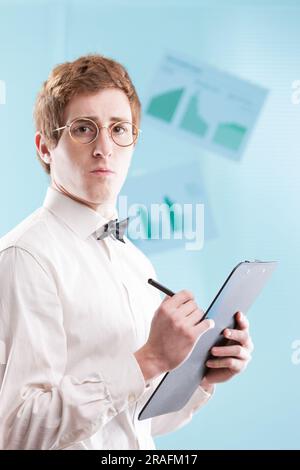 Un jeune homme dans un costume de bureau daté, peut-être un comptable subalterne, avec un bloc-notes, une chemise blanche et un noeud papillon, regarde tristement contre un générique, flou o Banque D'Images