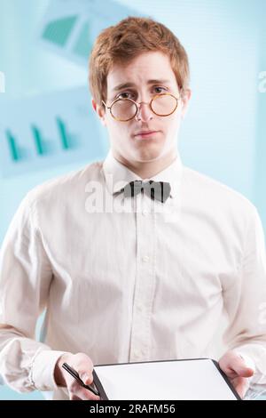 Un jeune homme un peu énerve, légèrement servile dans un costume de bureau daté, encombrant d'un bloc-notes, regarde malheureusement. Sa chemise blanche et son noeud papillon suggèrent qu'il peut b Banque D'Images