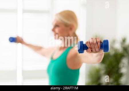 Femme sénior sportive motivée avec haltères à la maison Banque D'Images