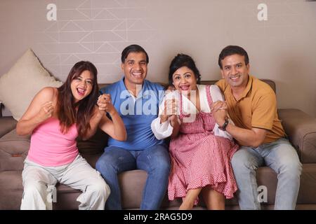 Heureux amis indiens couples assis sur un canapé appréciant regarder le match à la télévision et célébrer les moments gagnants. Banque D'Images
