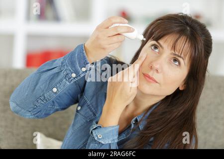 une jeune femme appliquant des eyedrops Banque D'Images