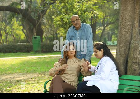 Docteur examinant les patients dans le parc de la ville parmi les verts assis sur le banc sous l'arbre. Banque D'Images