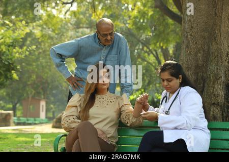 Docteur examinant les patients dans le parc de la ville parmi les verts assis sur le banc sous l'arbre. Banque D'Images