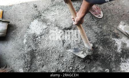 Travailleur asiatique utilisant la houe pour mélanger la puissance du ciment avec le sable Banque D'Images