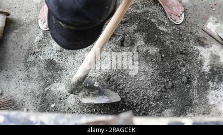 Travailleur asiatique utilisant la houe pour mélanger la puissance du ciment avec le sable Banque D'Images