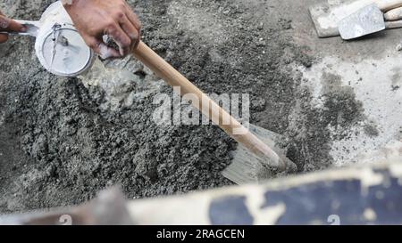 Travailleur asiatique utilisant la houe pour mélanger la puissance du ciment avec le sable Banque D'Images